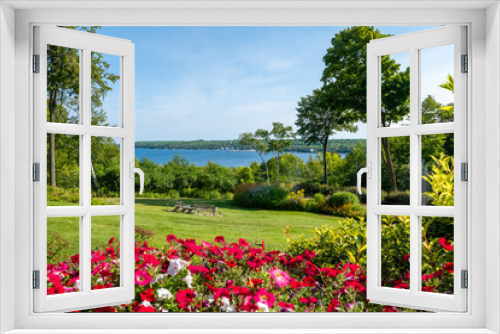 Fototapeta Naklejka Na Ścianę Okno 3D - Beautiful backyard scene with colorful flowers, green grass and other vegetation, a pond with a fountain, and a lake with blue water.
