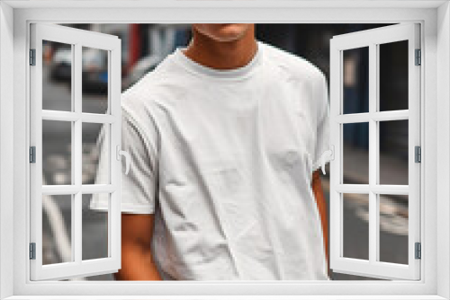 A young man in a classic oversized white blank T-shirt, blue jeans and sunglasses stands on a city street. Style and fashion clothing mock up template.