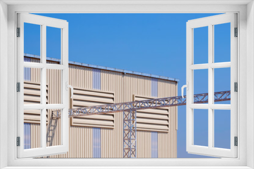 Fototapeta Naklejka Na Ścianę Okno 3D - Three aluminium louvers on corrugated metal wall with rain gutter and overhead electrical cable ladder of modern industrial factory building against blue clear sky background