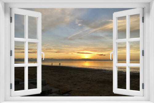 Fototapeta Naklejka Na Ścianę Okno 3D - On the beach, the golden early sunrise casts clouds on the sea horizon. Unrecognizable figures enjoy the view. Silhouettes