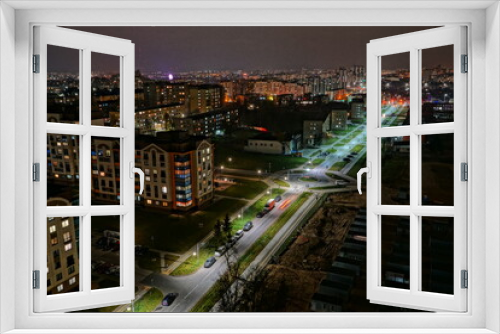 Fototapeta Naklejka Na Ścianę Okno 3D - The lights of the night city. View of the busy city traffic and the light from the headlights of cars at night. The lights are on in the windows of residential buildings.
