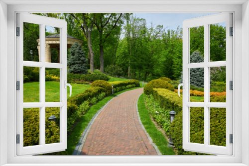 Fototapeta Naklejka Na Ścianę Okno 3D - Trimmed green bushes form a labyrinth along tiled pathways in the park,
