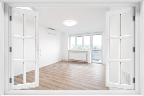 Fototapeta Naklejka Na Ścianę Okno 3D - A Bright, empty room with white walls, a large window, wooden floor, and a modern ceiling light. An air conditioner is mounted on the wall.