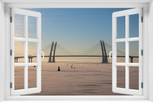 Fototapeta Naklejka Na Ścianę Okno 3D - View of the cable-stayed bridge over the Ship Fairway in St. Petersburg in winter.The Neva Bay of the Gulf of Finland is covered with ice, there are many fishermen on the ice engaged in winter fishing