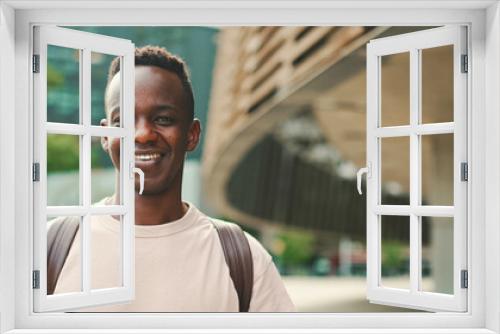 Young african student stands outside of university, looks at the camera and smiles, Panorama