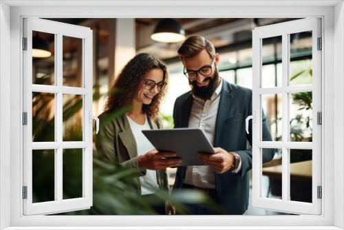 Smiling businesswoman and businessman using tablet device while discussing business-related data in the office.