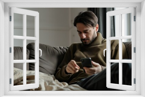 Portrait of an attractive man wearing casual clothes sitting on a couch at the living room with mobile phone. For commercial advertising