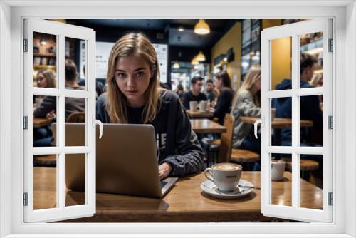 woman smiling and sitting at a table with a laptop and a cup of coffee. She is focused on her work. There are other people in the background, engaged in their own activities.