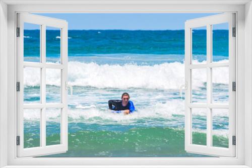 Fototapeta Naklejka Na Ścianę Okno 3D - Young man smiling with bodyboard, riding wave to shore, doing water sport, wearing sun shirt, seaside landscape, summer sunny day.