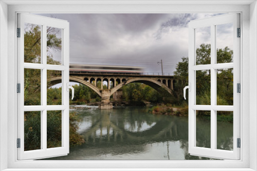 Fototapeta Naklejka Na Ścianę Okno 3D - Urban Motion: Speeding Train Across Cloudy River Bridge