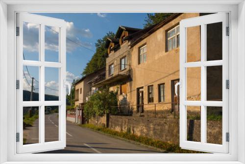 Fototapeta Naklejka Na Ścianę Okno 3D - A quiet residential road in Kulen Vakuf village in the Una National Park. Una-Sana Canton, Federation of Bosnia and Herzegovina. The buildings foreground right are abandoned. Early September