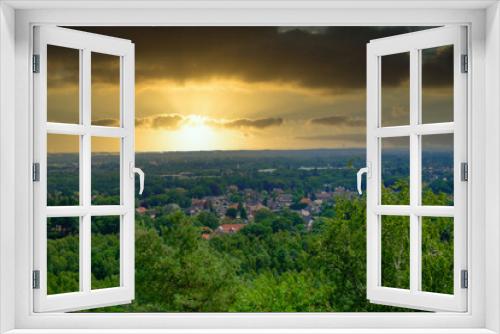 Fototapeta Naklejka Na Ścianę Okno 3D - This evocative image captures the dramatic beauty of a suburban landscape bathed in the golden light of a setting sun. The heavy cloud cover adds a dramatic contrast to the sun's bright rays piercing