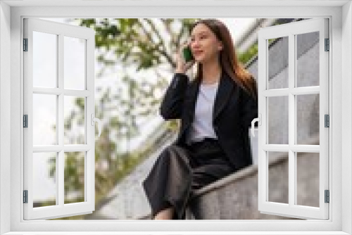 Asian businesswoman sitting and using phone outdoor, with a tumbler beside her