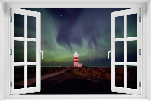 Fototapeta Naklejka Na Ścianę Okno 3D - Majestic lighthouse situated on a rocky shore illuminated with a bright green light