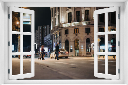 Fototapeta Naklejka Na Ścianę Okno 3D - People crossing the street in a bustling city nighttime setting.
