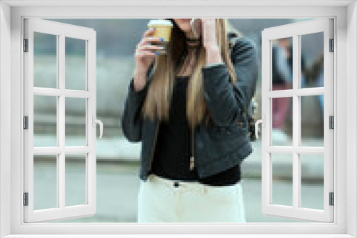 Young woman on the phone with a coffee. Dreamy hipster girl enjoying leisure time while walking at spring urban setting with gadget