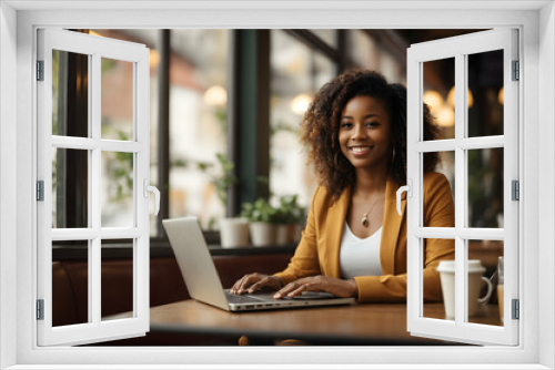 Image of happy woman using laptop while sitting at cafe. Young african american woman sitting in a coffee shop and working on laptop.blur background. 