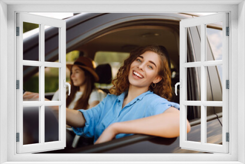 Two trendy attractive young woman singing along to the music as they drive along in the car through town. Beautiful female friends in the car enjoy a car trip together.