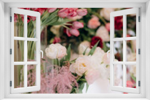 Fototapeta Naklejka Na Ścianę Okno 3D - The wedding reception is decorated with glass vases, filled with white and pink tulips, surrounded by burning candles, which creates an intimate romantic atmosphere, close-up. Photo zone for a couple 
