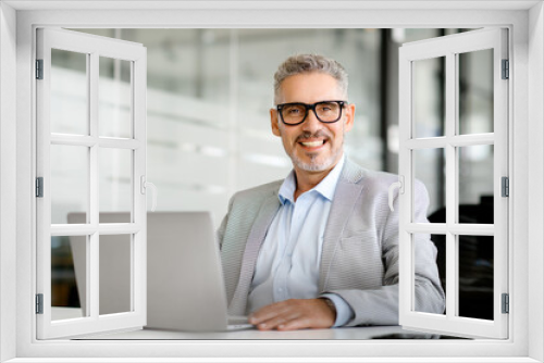 Confident businessman is captured with a broad, engaging smile as he works in an airy, well-designed corporate space, emphasizing approachability and professionalism