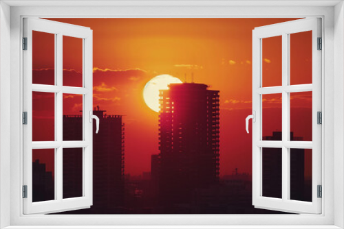 Sun setting behind tall city buildings creating a silhouette against the sky. Copy space. Background.