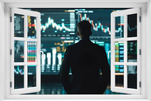 A man stands in front of a computer monitor displaying financial data. He is focused and attentive, possibly analyzing the information on the screen. Concept of seriousness and concentration