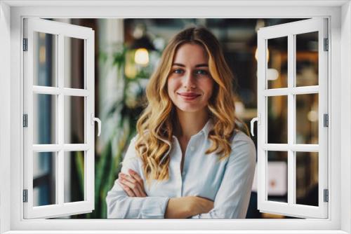 
Confident businesswoman stands in office with arms crossed, smiling at the camera.