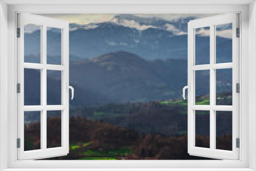 Fototapeta Naklejka Na Ścianę Okno 3D - A scenic view over the valley and the mountains in the background. Green sun lit patches of grass in the valley beneath in the sunset.
