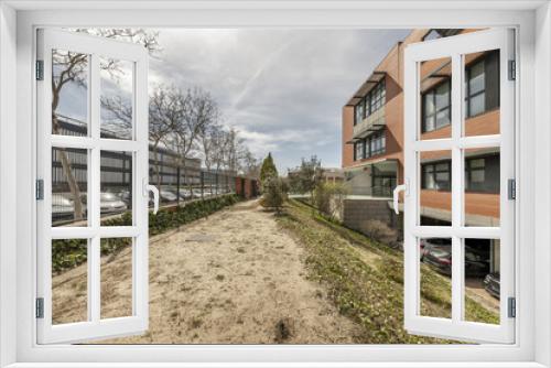 Fototapeta Naklejka Na Ścianę Okno 3D - Front image of the facade of the office building with a light brown brick wall combined with black metal windows, ground floor parking and gardens