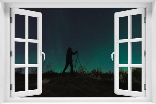 Fototapeta Naklejka Na Ścianę Okno 3D - A landscape astro photographer with a camera on a tripod takes pictures of the starry sky and the northern lights.