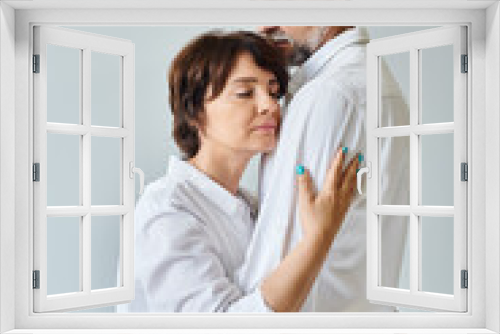 Attractive middle aged woman hugging mature man in white shirt with love on grey background