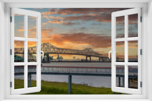 Fototapeta Naklejka Na Ścianę Okno 3D - The Horace Wilkinson Bridge over the flowing waters off the Mississippi River with boats on the water, lush green grass and clouds at Louisiana Memorial Plaza in Baton Rouge Louisiana USA