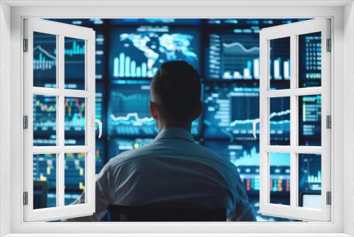 A man is sitting in front of a computer monitor with many graphs and numbers