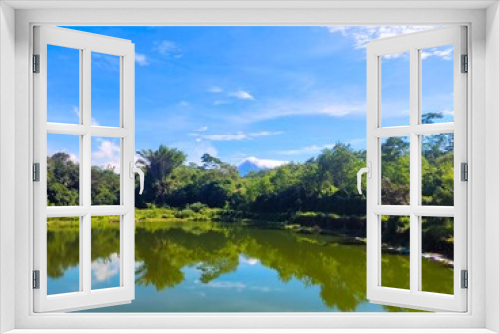 Fototapeta Naklejka Na Ścianę Okno 3D - A beautiful scene of a pond full of water with a clean, fresh and green environment. Merapi mountain and bright blue sky in the background.