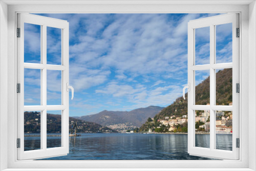 Lago di Como. Beautiful view of the lake of Como against Alps mountains and blue cloudy sky background on a sunny winter day in the province of Milan in Lombardy, Italy. Wonderful travel destinations