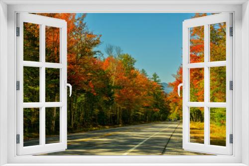 Fototapeta Naklejka Na Ścianę Okno 3D - A road among a colorful autumn forest leading to the mountains on a sunny warm autumn day. Traveling around the USA.