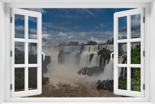 Fototapeta Naklejka Na Ścianę Okno 3D - Beautiful tropical waterfall landscape. Cascading streams collapse from ledges into the bed of a stormy river. Splashes, fog. Clouds in the blue sky. Lush green vegetation. Iguazu Falls. Argentina.