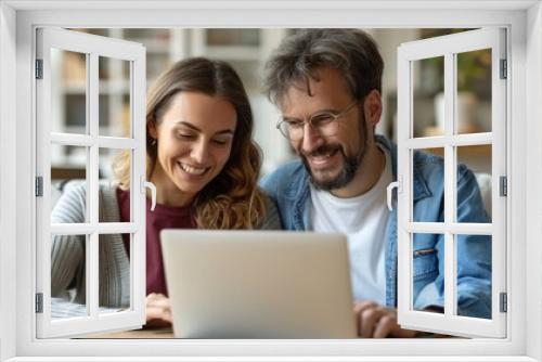 A man and a woman are sitting together, focused on a laptop screen in front of them