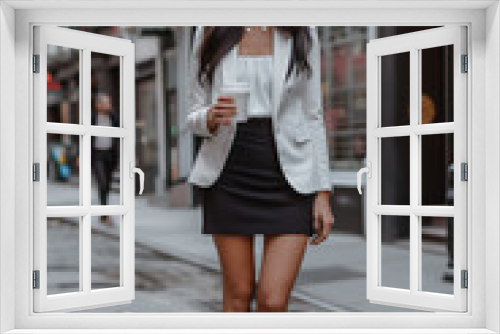 A smiling woman with long brown hair, dressed in professional business attire, walks to work over a cobblestone street while holding a cup of coffee.