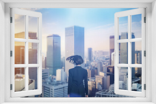 日本の街・都市・朝日を受けたオフィスビル群を前に佇み風を受けて髪をなびかせる会社員の女性の出勤　就職・ビジネス・はじまり・決意・目標・挑戦のイメージ