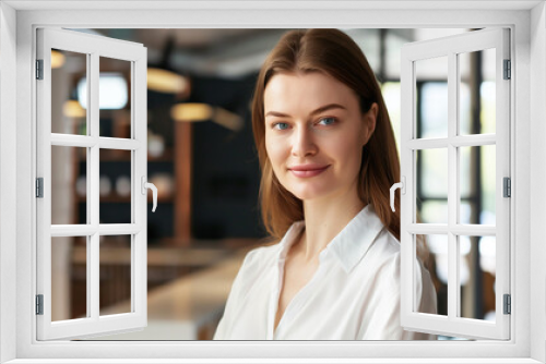 Beautiful, tanned businesswoman with a soft smile, neat loose hair, and light makeup, in a bright shirt, hands in pockets, in front of a blurred office setting. She looks happy and successful.