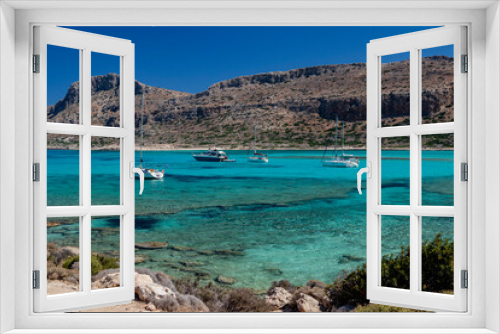 Fototapeta Naklejka Na Ścianę Okno 3D - Several boats float in the water close to a towering mountain in a picturesque scene with nature elements like trees and plants, set against a clear sky. Crete. Balos. Greece.
