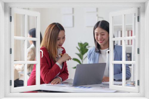 Two businesswomen collaborate on a project using a laptop in a modern office environment. Teamwork, productivity, and professional discussion.