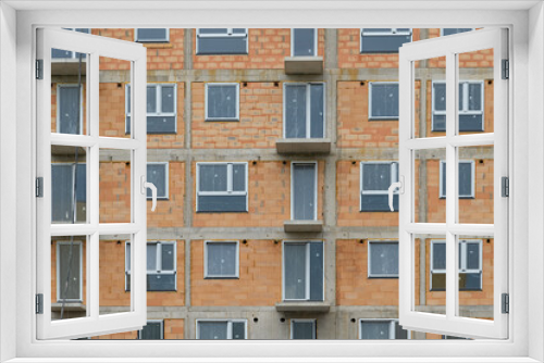 Fototapeta Naklejka Na Ścianę Okno 3D - red clay ceramic thermo brick multi-story building before insulation and cladding. New windows installed, reflecting the real estate market.