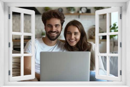 A smiling couple uses a laptop together while sitting on a couch in their living room