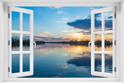 Fototapeta Naklejka Na Ścianę Okno 3D - The sun is casting a warm golden glow as it sets over the calm waters of a lake, creating a serene and magical atmosphere.