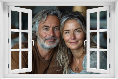 two happy casual middle aged couple with grey hair sitting on a sofa in a living room