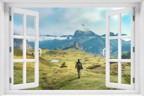 Fototapeta Naklejka Na Ścianę Okno 3D - Young man hiking up a grassy hill in the mountains under a cloudy sky, surrounded by lush greenery with a vast landscape spreading in the horizon. High quality photo