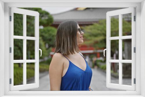 Cheerful, beautiful hispanic woman with glasses joyfully exploring and admiring the majestic senso-ji temple as she casually strolls, looking around with awe and a confident smile.