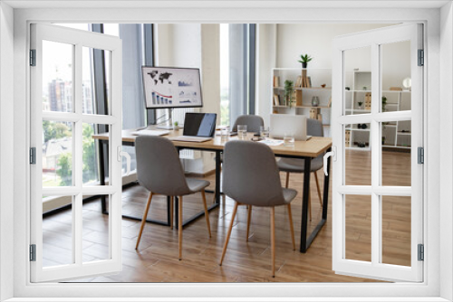 Spacious and bright office conference room with a city view, featuring chairs, a desk, digital screens, and modern decor.